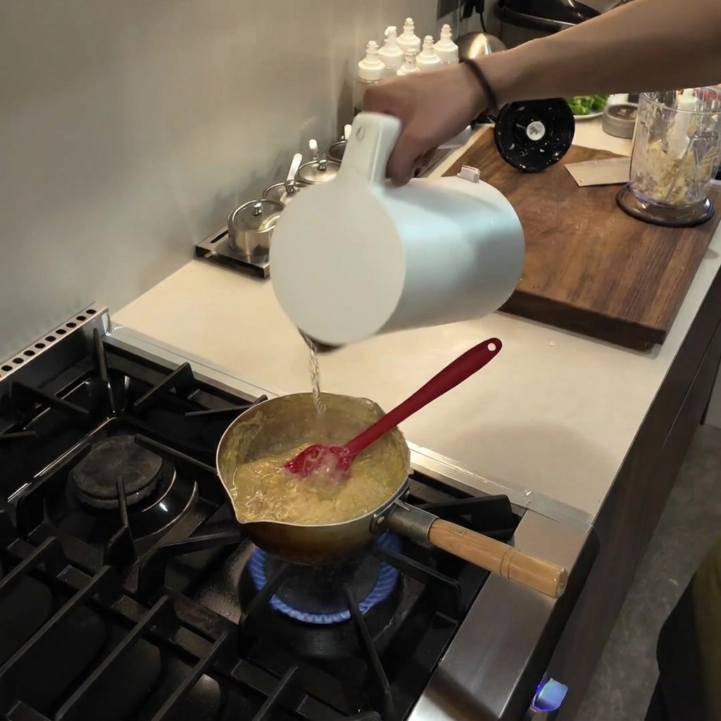 Versement deau à partir dune pichet blanc dans une casserole contenant un mélange de fufu qui épaissit et mijote.