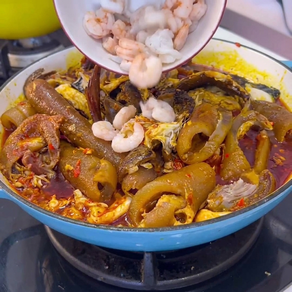 Un bol de crevettes blanches décortiquées ajoutées dans une casserole de cuisson remplie de peau de porc braisée et de sauce chili.