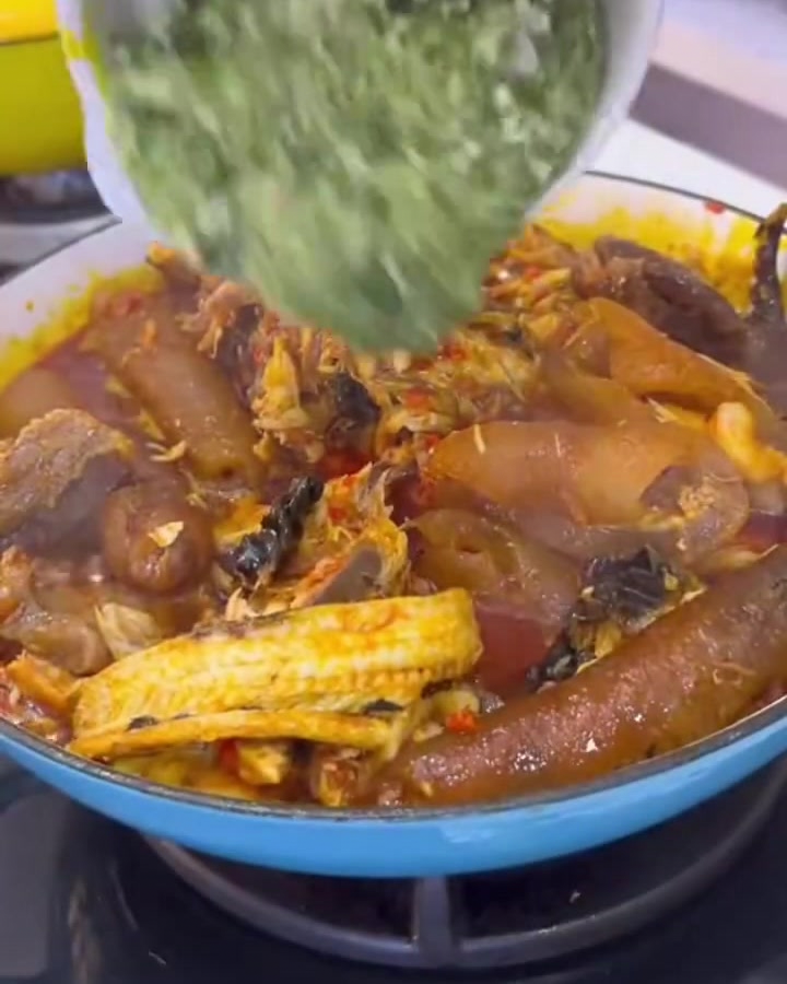 Des gombos verts finement hachés versés dun bol blanc dans une riche casserole bouillonnante de viandes et de sauce.