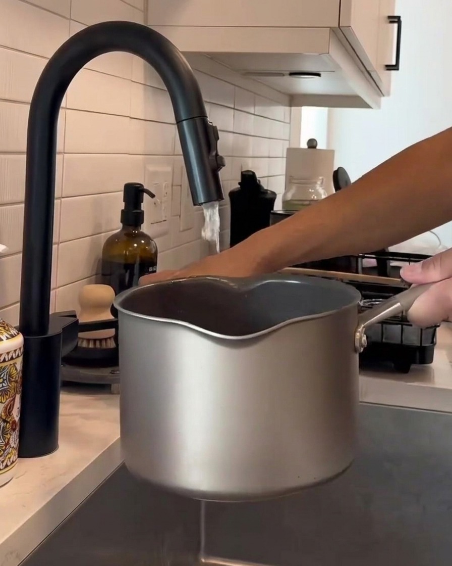 Mains remuant du riz blanc dans une casserole en métal sous un robinet deau courante.
