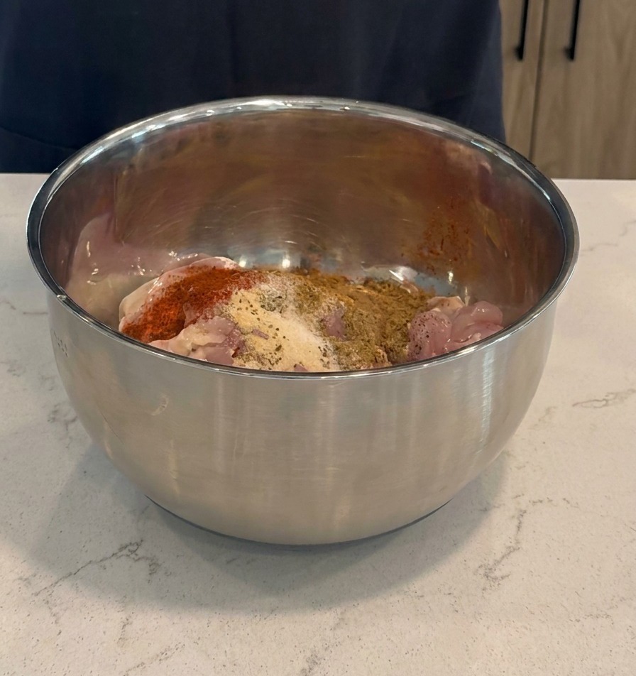 Ajout dune marinade rouge foncée et dépices sèches sur des cuisses de poulet crues dans un bol en acier inoxydable.