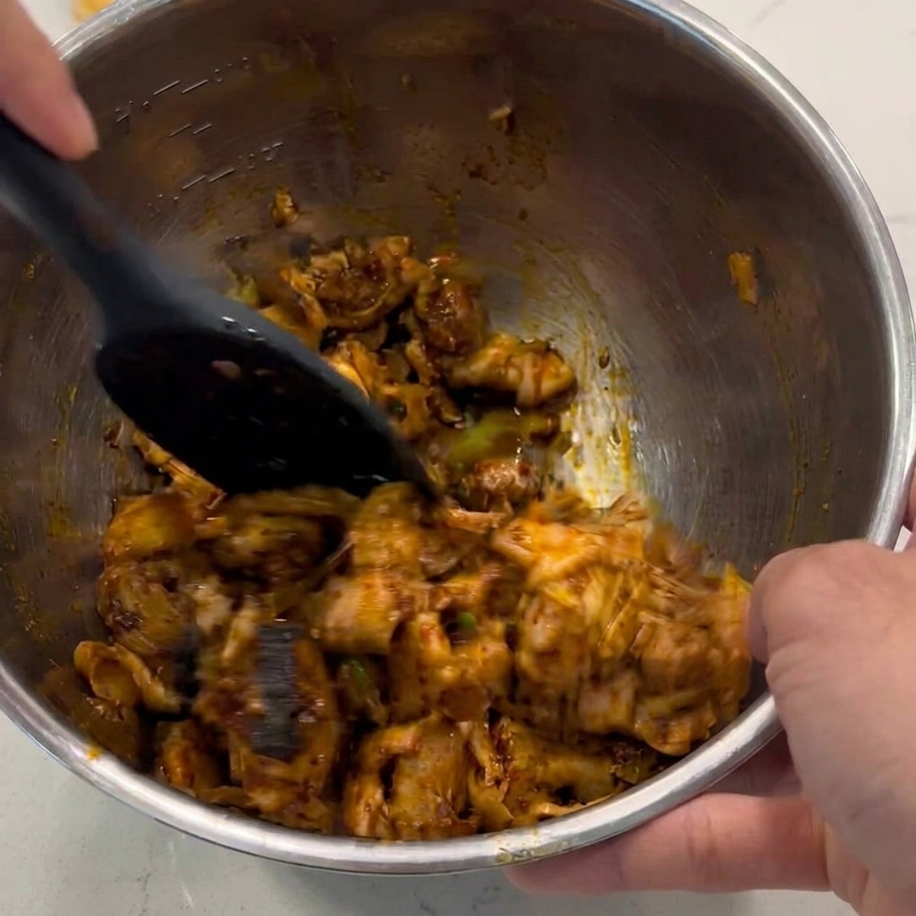 Une spatule noire mélangeant et remuant des morceaux de poulet en dés pour les enrober dune sauce brune brillante dans un bol en métal.