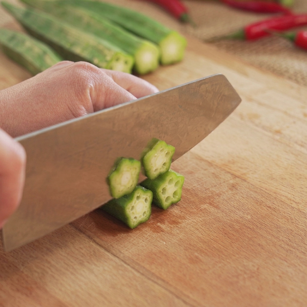 Des gombos verts coupés en rondelles en forme détoile sur une planche à découper en bois avec un couteau de cuisine.