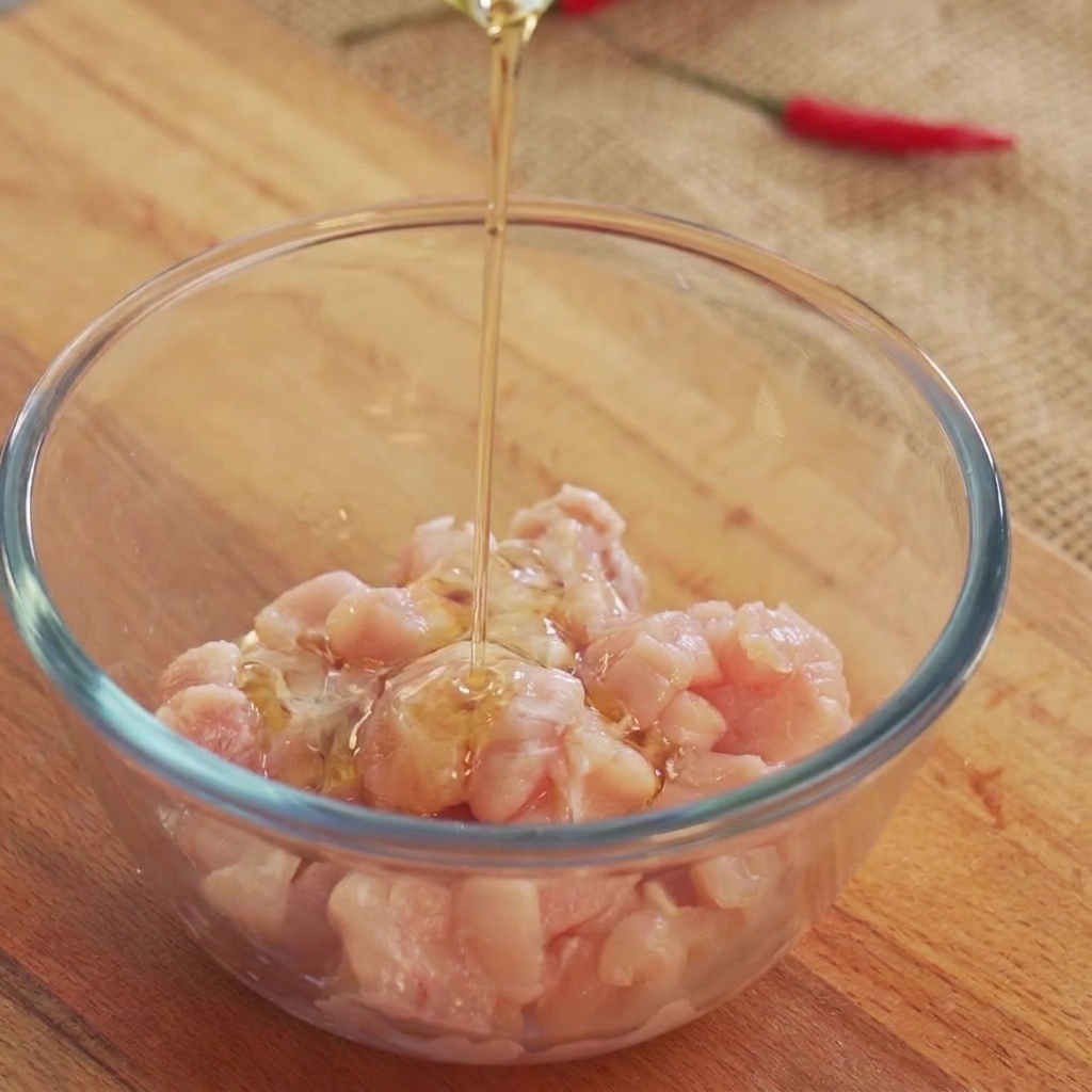 De lhuile de cuisson versée par le dessus sur des morceaux de poulet cru à lintérieur dun bol en verre.