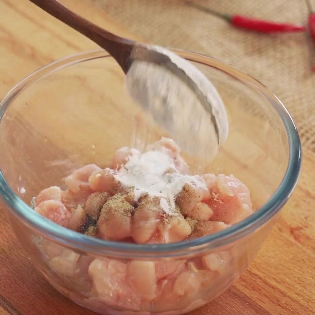 Du vin de cuisine et des poudres dassaisonnement blanches saupoudrés sur des cubes de poulet cru dans un bol en verre.