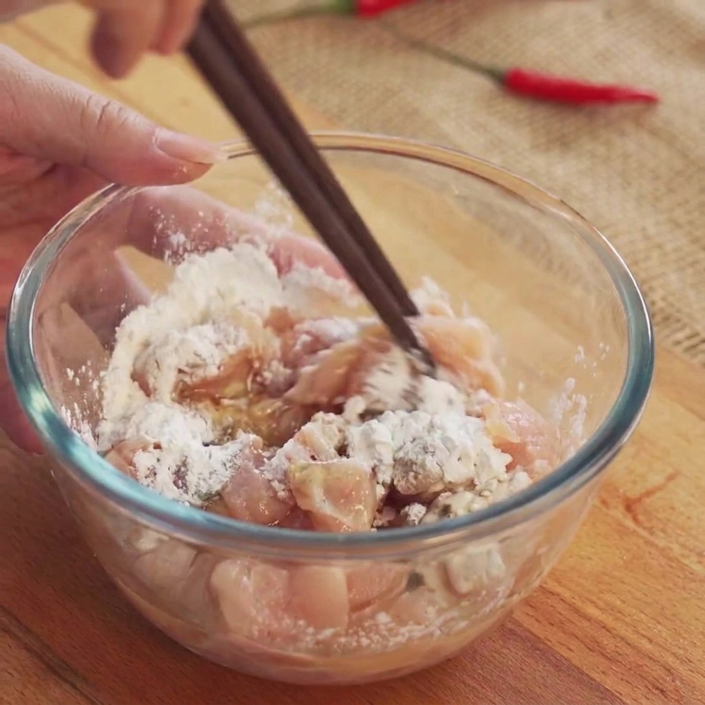 Des cubes de poulet remués avec des baguettes à lintérieur dun bol en verre transparent pour mélanger la marinade.
