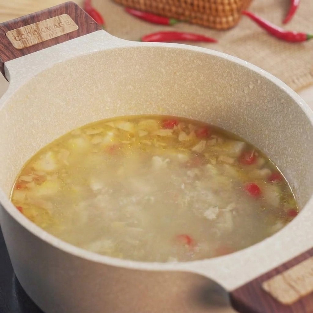 Des tranches de gombos verts jetées dans une casserole remplie de bouillon de poulet frémissant.