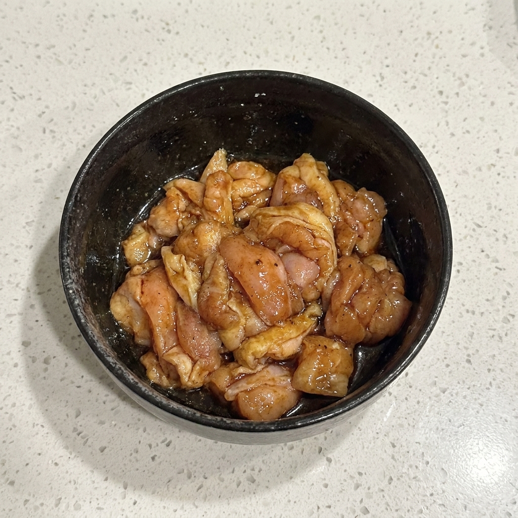 Des morceaux de poulet cru marinés mélangés soigneusement dans un bol noir.