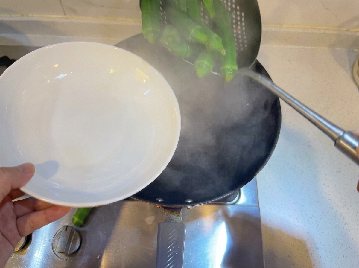 Des gombos entiers blanchis dans une casserole deau bouillante à laide dune écumoire.