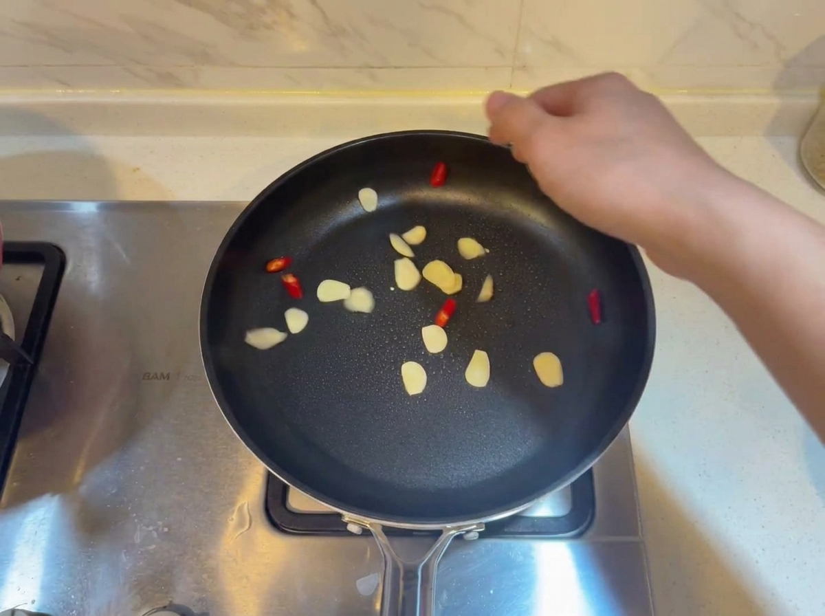 Des tranches dail et des morceaux de piment rouge grésillant dans une poêle chaude et huilée.