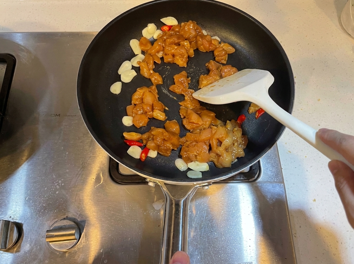 Des morceaux de poulet marinés en dés cuits dans une poêle avec de lail et des piments.