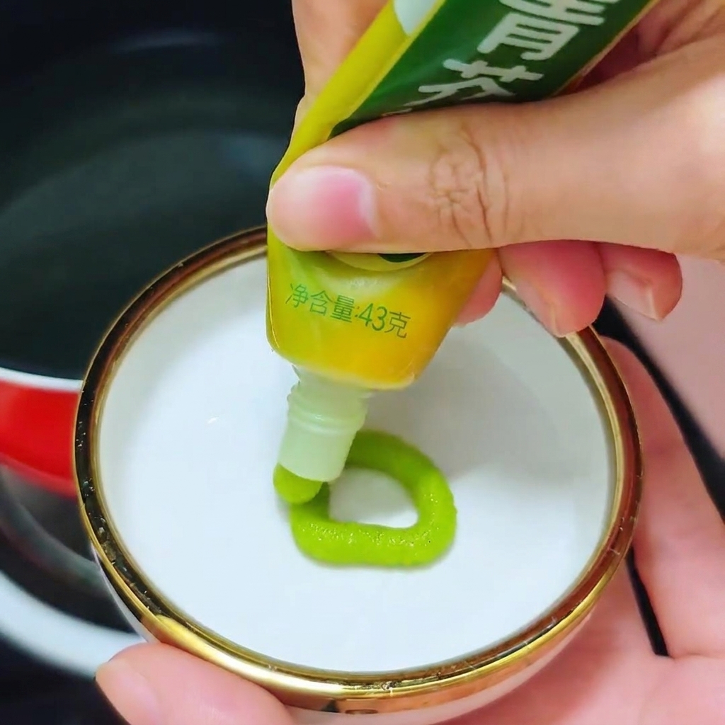 Une personne pressant un anneau de pâte de wasabi vert vif dun tube dans une petite coupelle blanche.