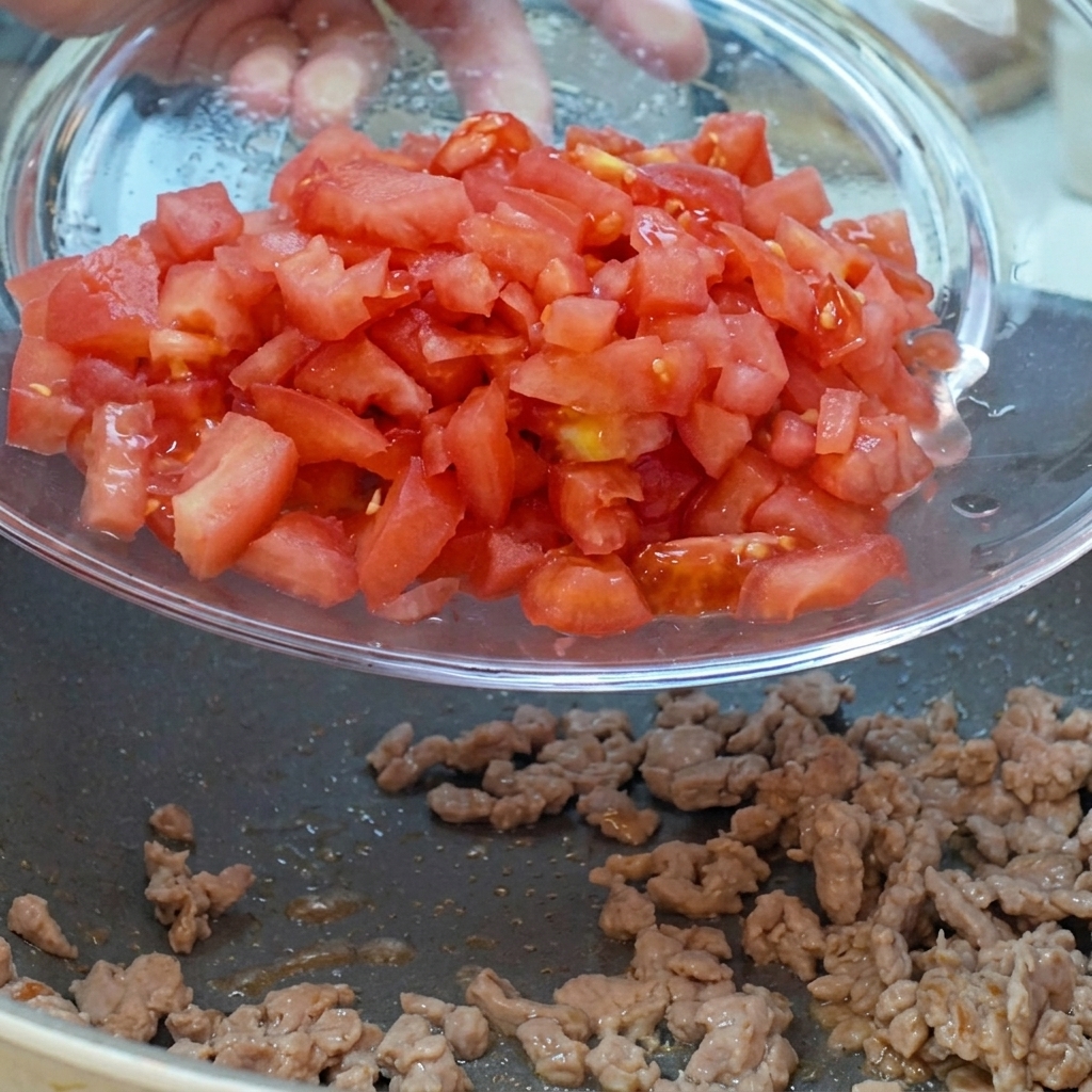 Dés de tomates et doignons rouges versés dun bol en verre dans la poêle contenant la viande.