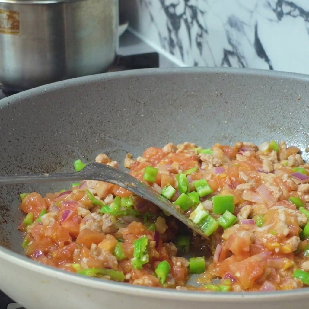 Eau versée dun récipient dans une poêle remplie dun mélange de viande hachée et de légumes en dés.
