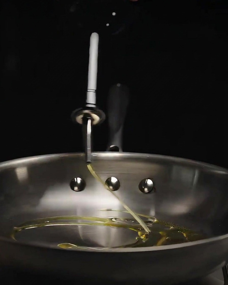 De lhuile dolive versée dune bouteille en verre dans une poêle en acier inoxydable brillante.