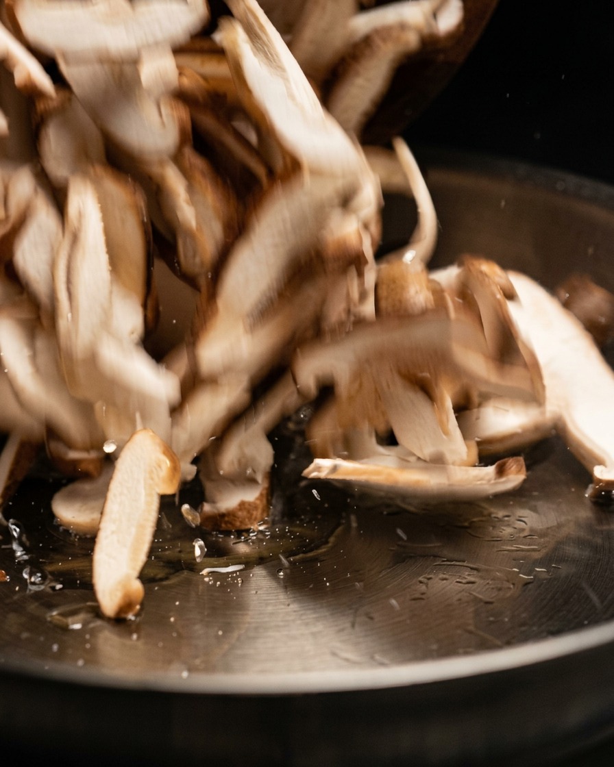 Des tranches de champignons crus mélangées et ajoutées dans une poêle chaude.