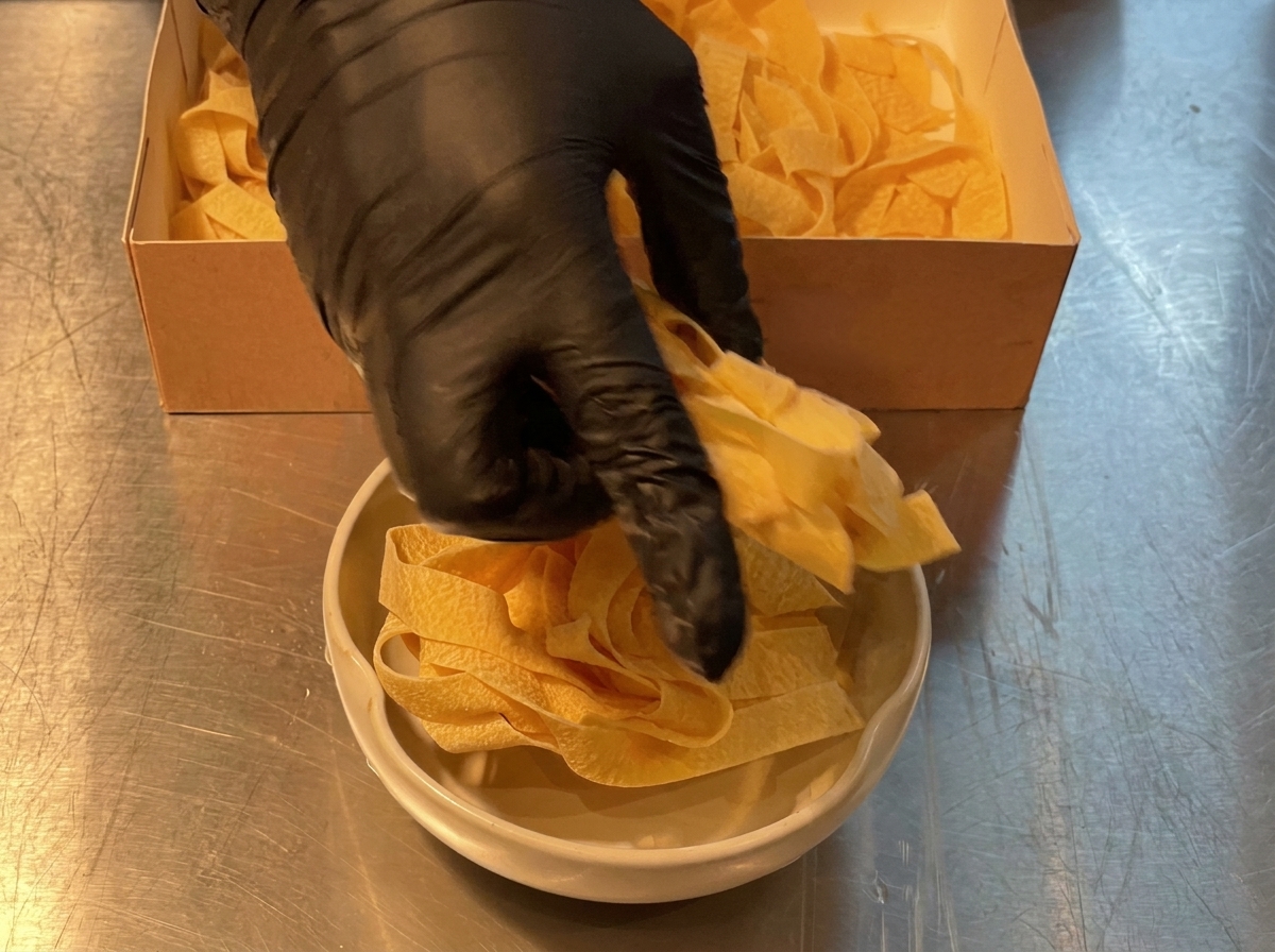 Pâtes larges versées dune boîte en carton dans une grande casserole.
