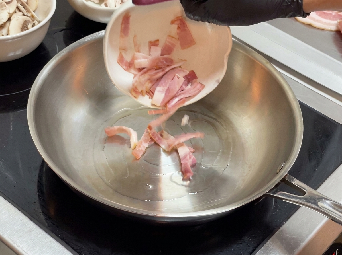 Lardons versés dun petit bol blanc dans une poêle en acier inoxydable.