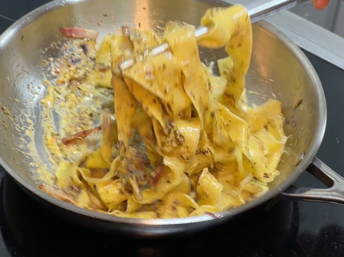 Une pince mélangeant les pâtes et la sauce dans une poêle sur la cuisinière.