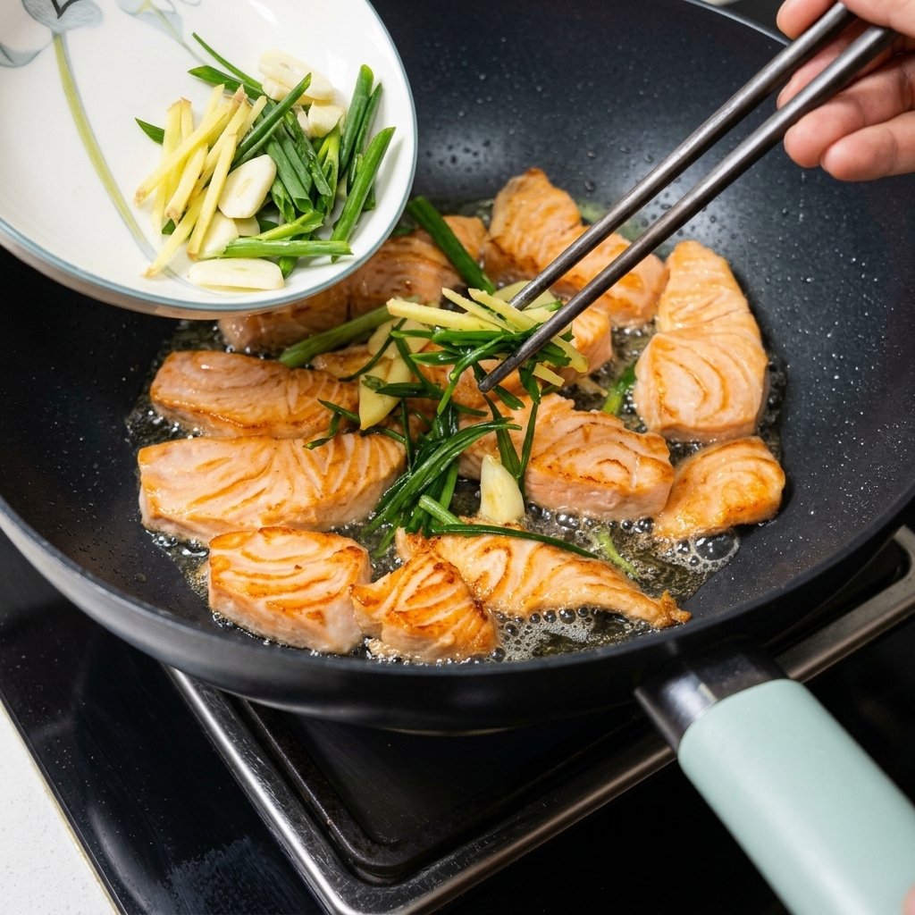 Cébettes et gingembre sautés reversés dans la poêle contenant les morceaux de saumon.