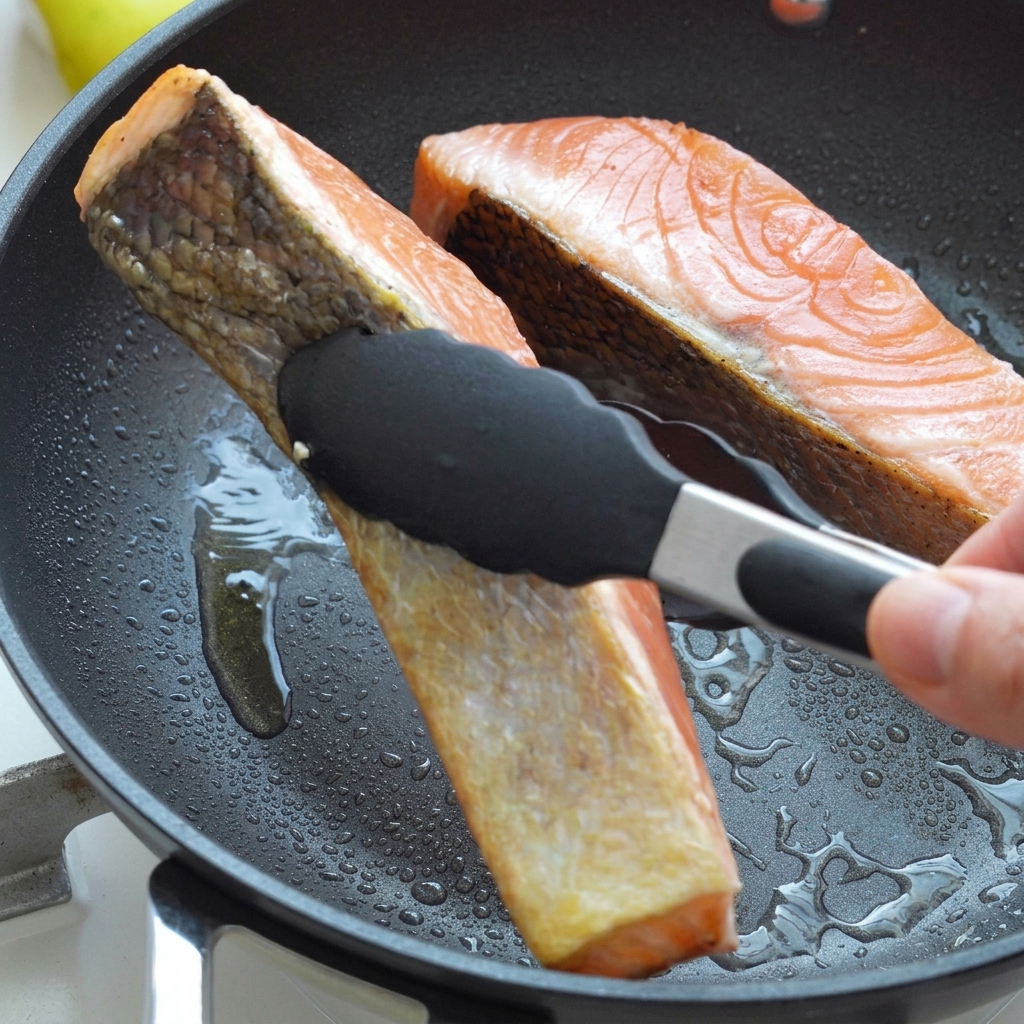 Filets de saumon retournés avec des pinces noires dans une poêle chaude avec de lhuile, montrant une peau saisie dorée.