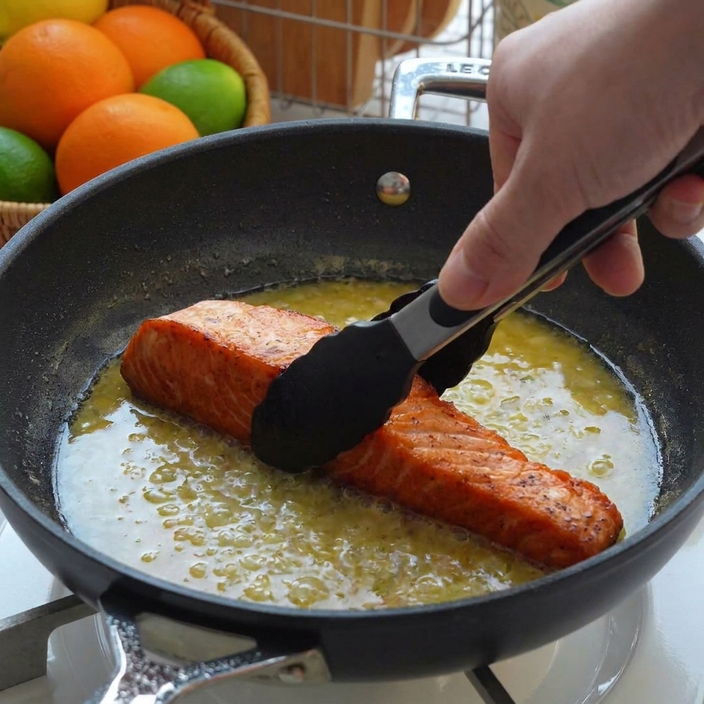 Filets de saumon saisis replacés dans une poêle remplie de sauce au beurre de citron à laide de pinces noires.
