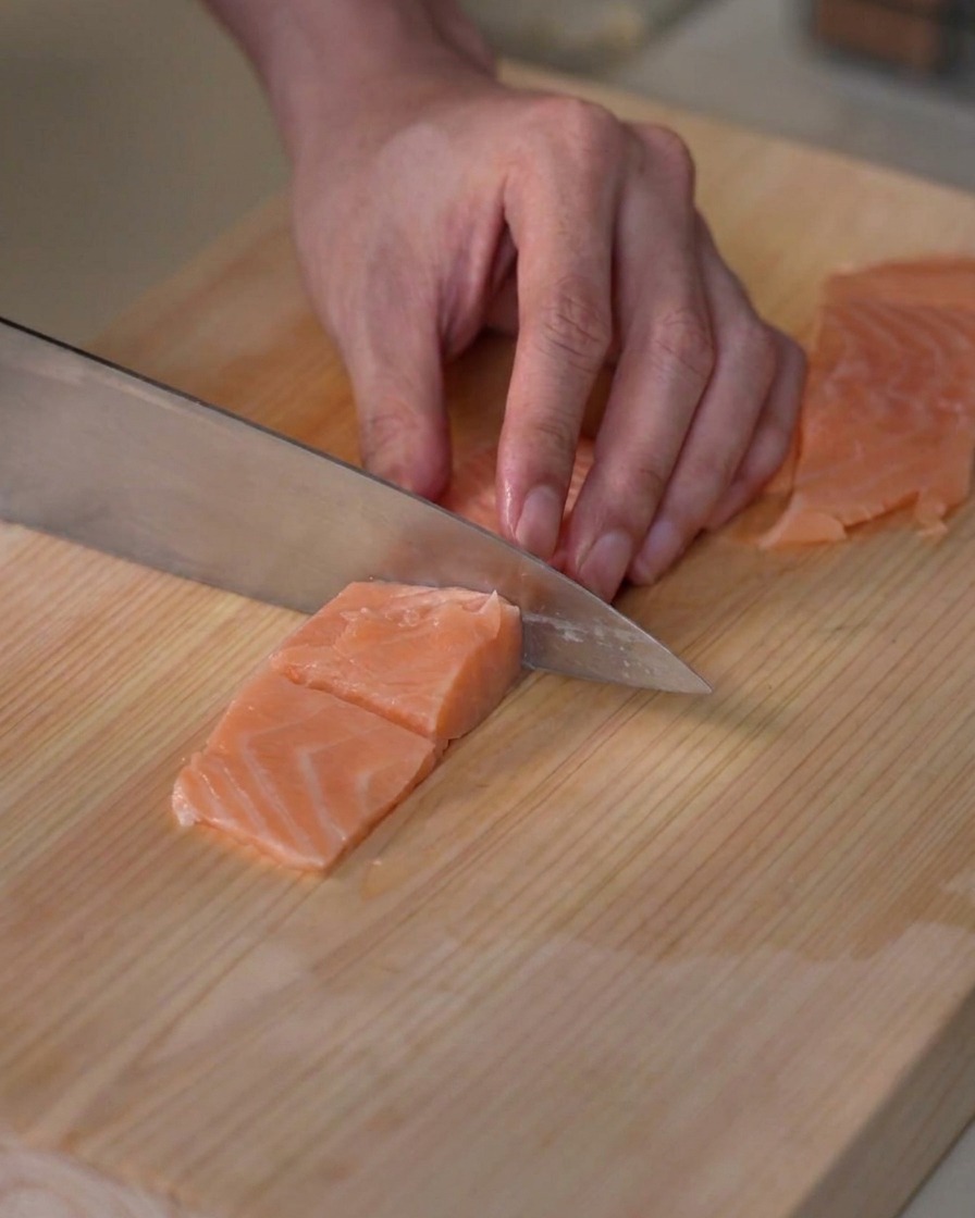 Un filet de saumon frais découpé en petits cubes réguliers sur une planche à découper en bois.
