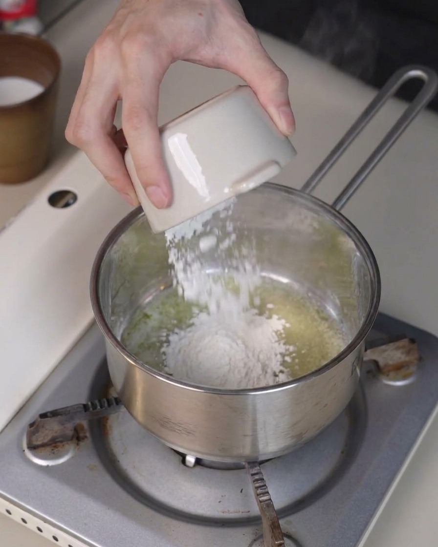 De la farine versée dun petit bol dans le beurre fondu dune casserole, tout en étant remuée avec une spatule.