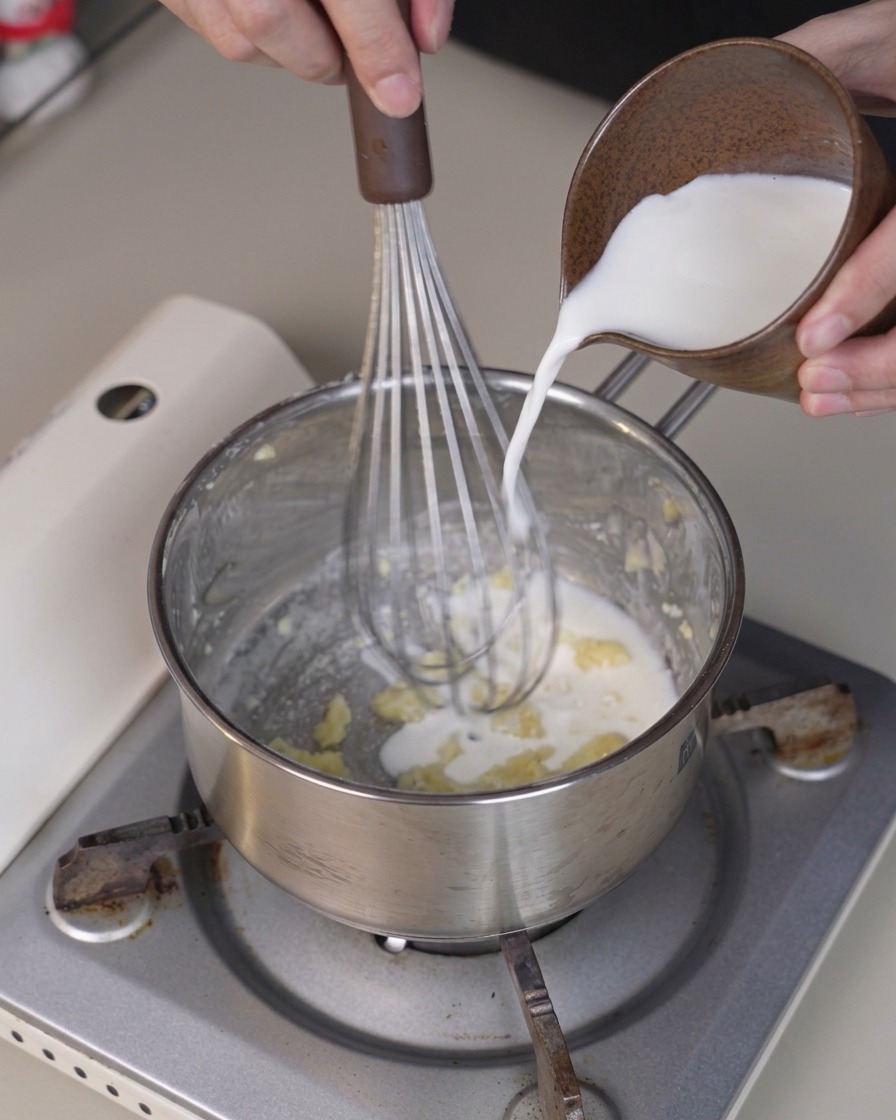 Du lait froid versé dune petite pichet dans une casserole tandis quun fouet mélange la préparation.