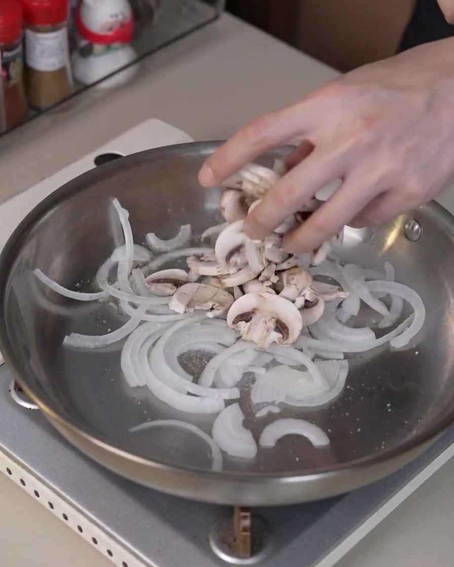 Des champignons de Paris tranchés ajoutés dans la poêle avec les oignons pour cuire et rendre leur eau.