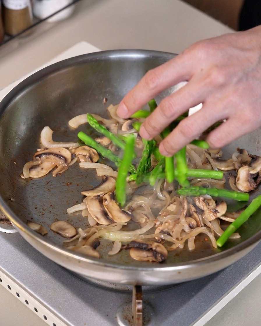 Des morceaux dasperges vertes mélangés dans la poêle contenant les oignons et les champignons sautés.