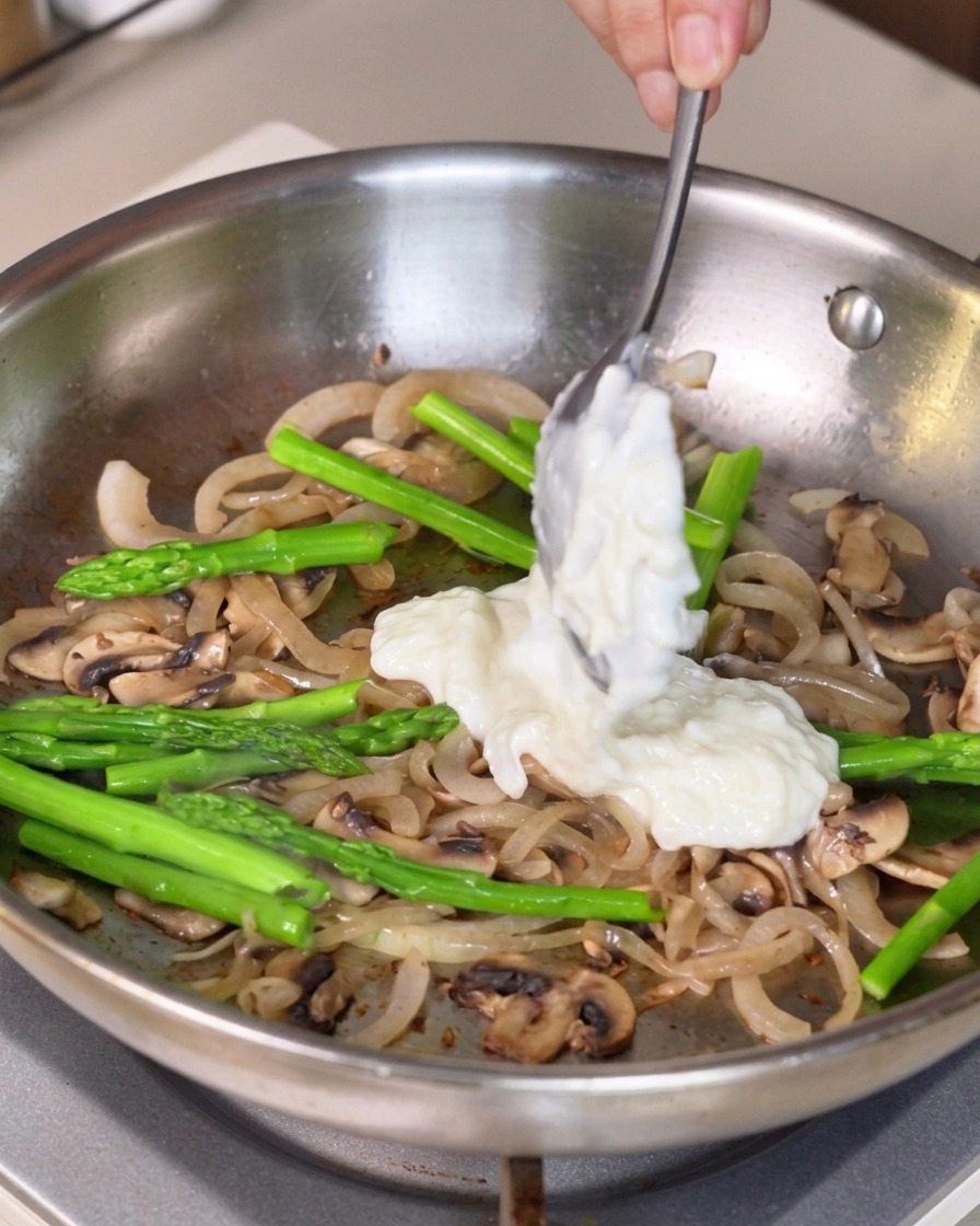 Une sauce blanche épaisse prélevée à la cuillère et ajoutée aux légumes dans la poêle.