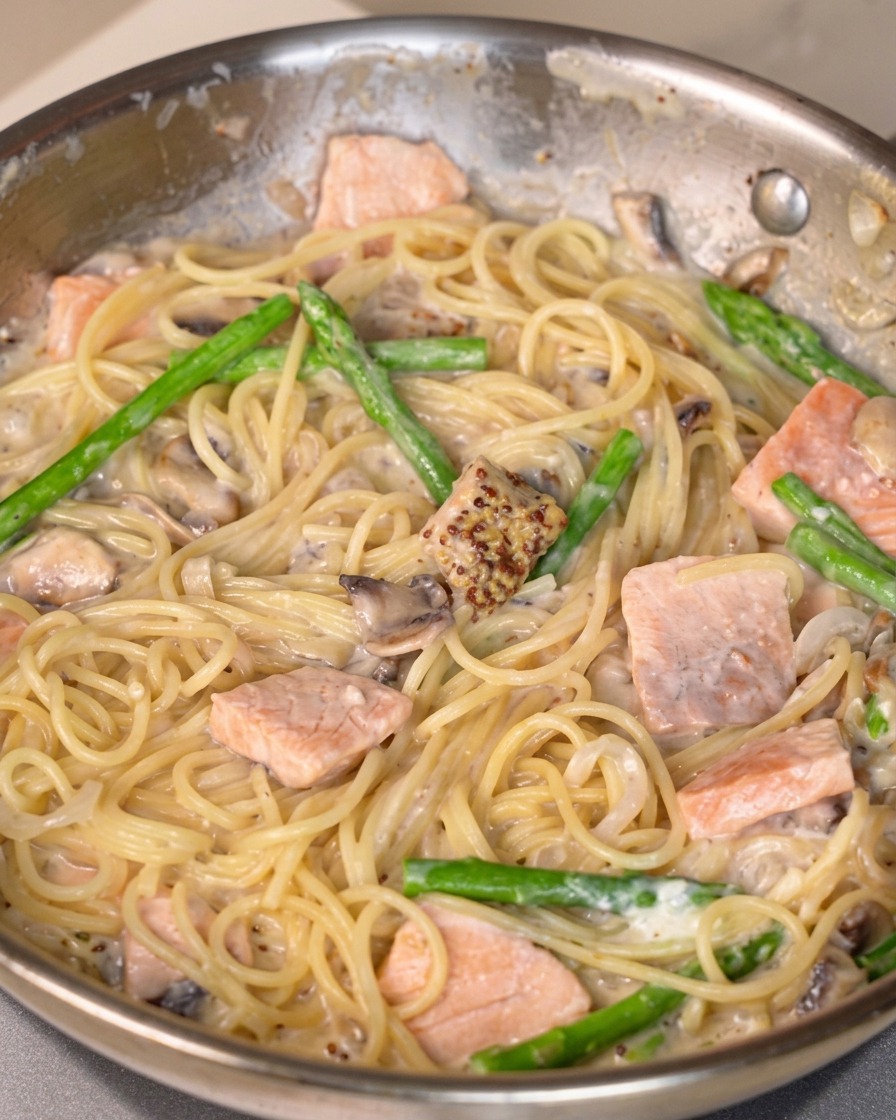 De la sauce moutarde, du sel et du poivre incorporés dans une poêle de pâtes au saumon crémeuses.