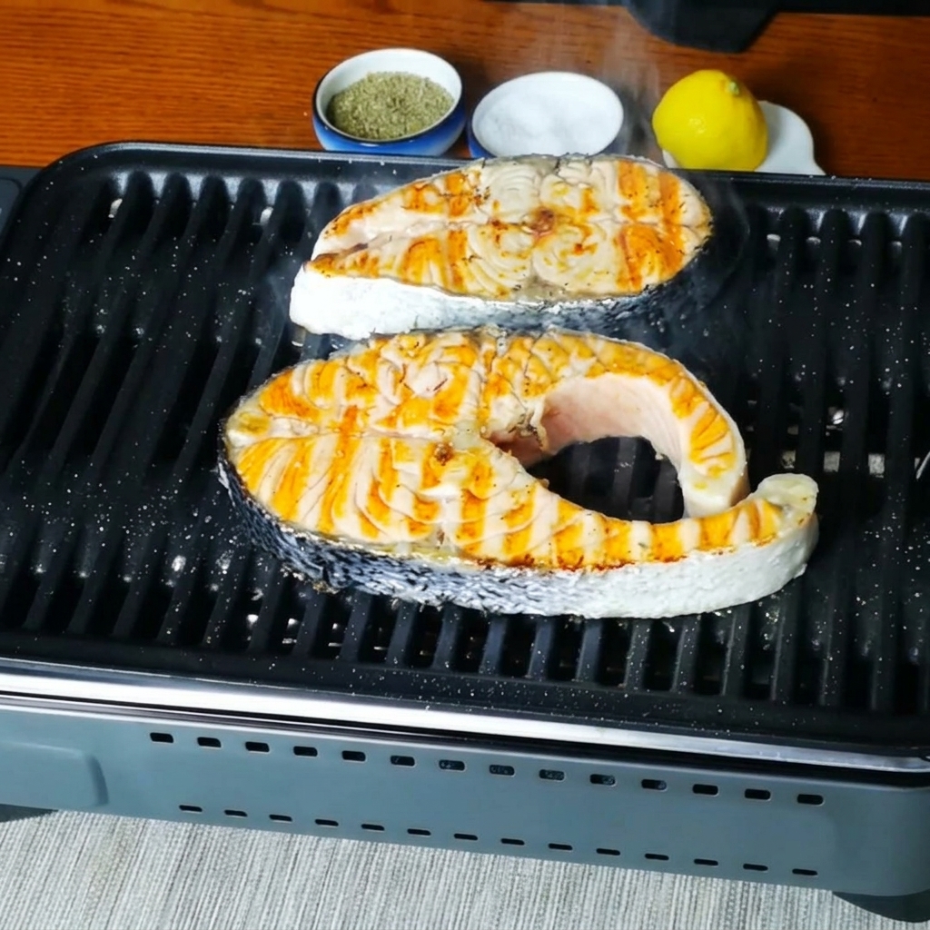 Gros plan sur des darnes de saumon grésillant sur la poêle à griller après avoir été assaisonnées.