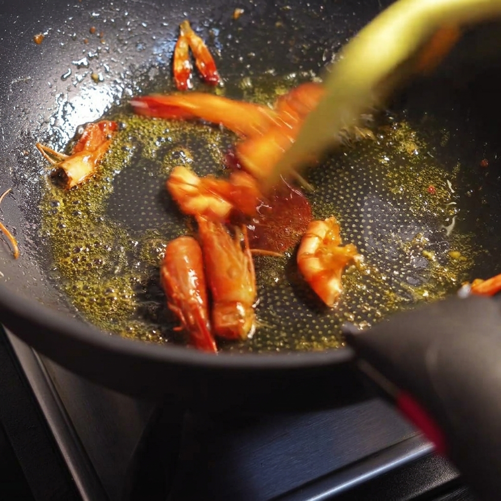 Têtes et carapaces de crevettes sautées à la poêle, libérant une huile rouge orangé.