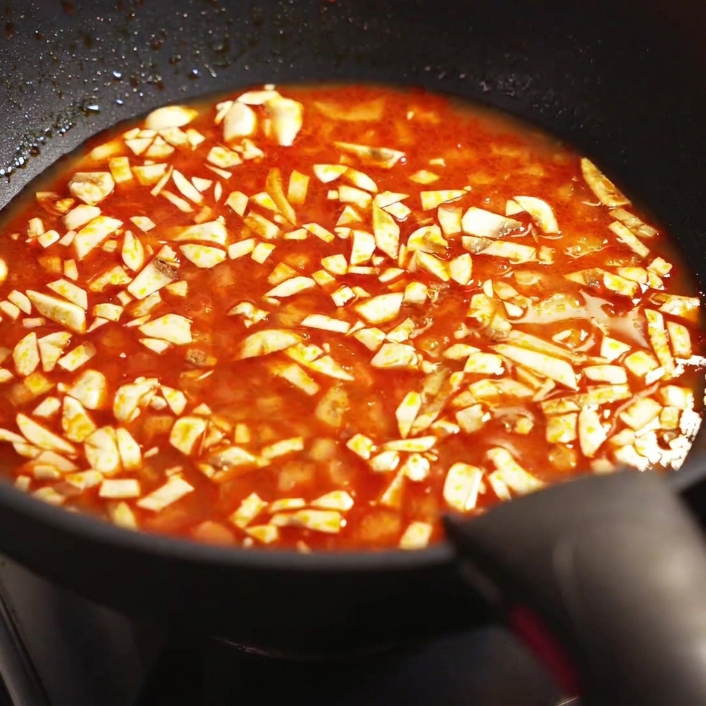 Gros plan de champignons mijotant dans un bouillon rouge assaisonné à lintérieur dune poêle.