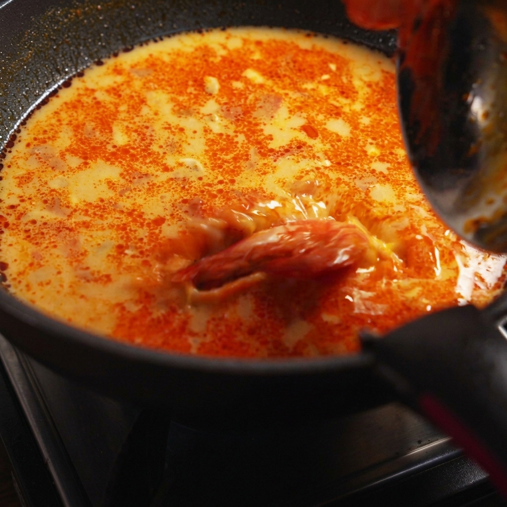 Spaghettis cuits, crevettes et coriandre fraîche incorporés dans la poêle de sauce frémissante.