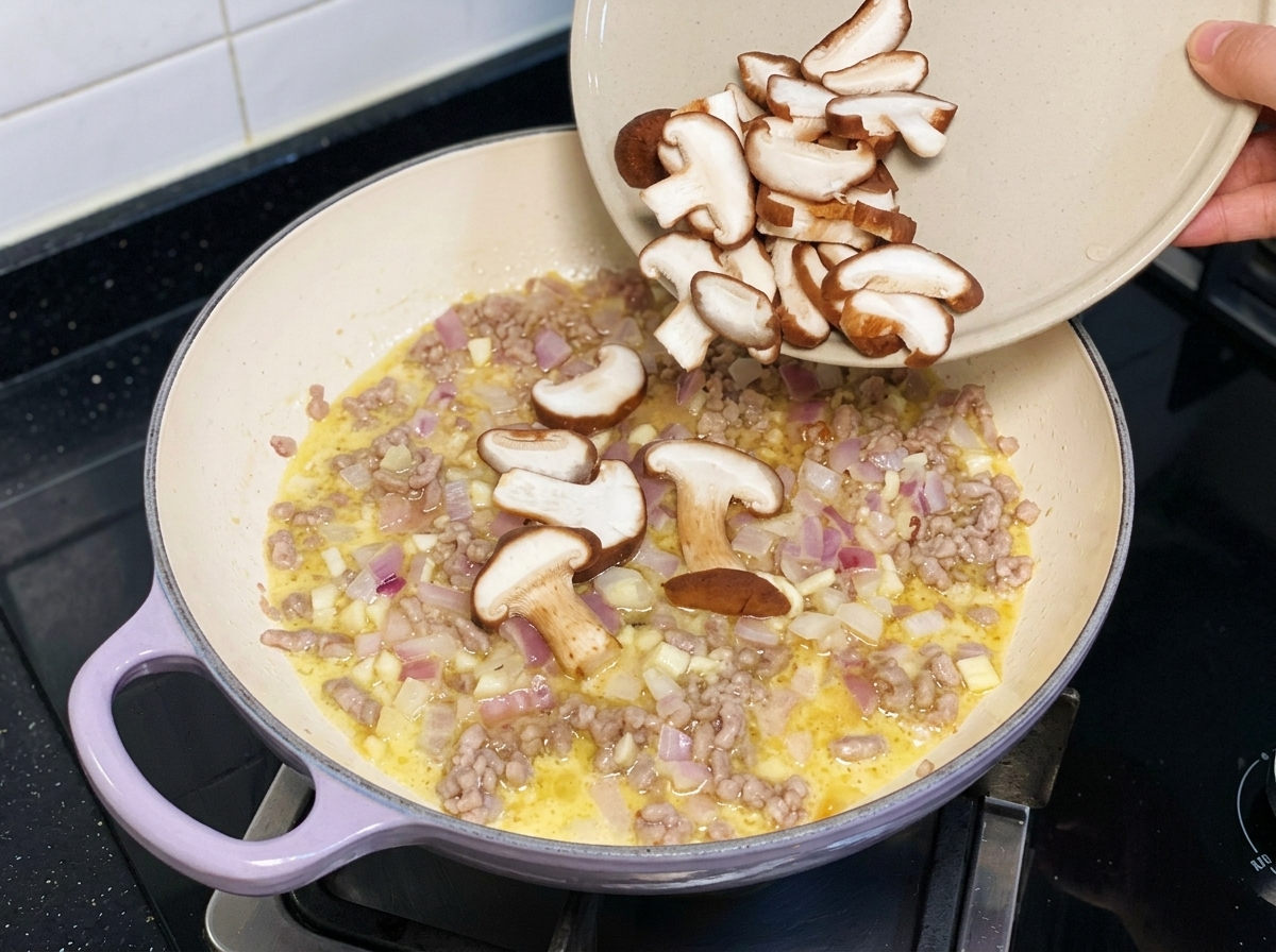 Des tranches de champignons shiitake frais versées dune assiette dans une poêle avec le porc haché et les oignons.