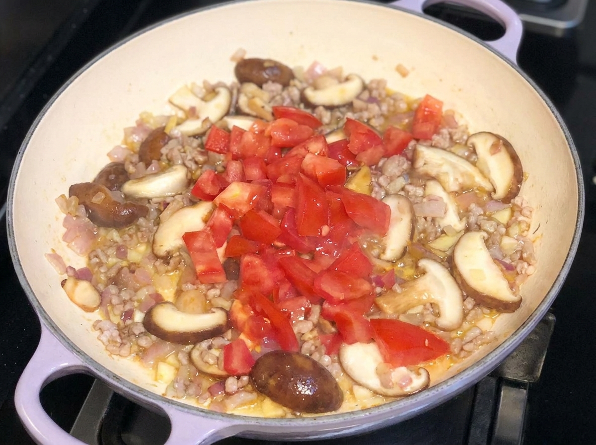 Des tomates fraîches coupées en dés ajoutées sur le dessus du mélange sauté de porc, doignons et de champignons dans une poêle.