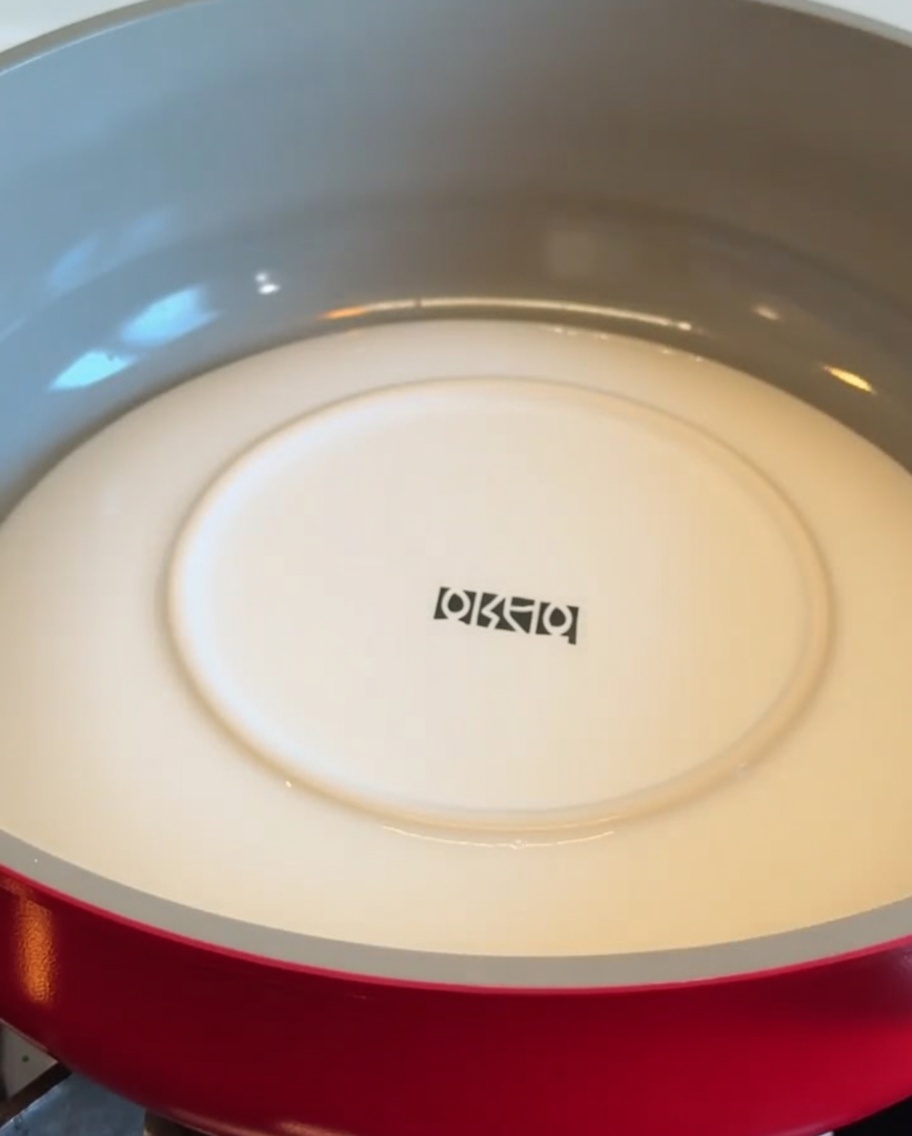 Une assiette blanche placée à lenvers dans une poêle rouge pour retourner une croûte de pommes de terre.
