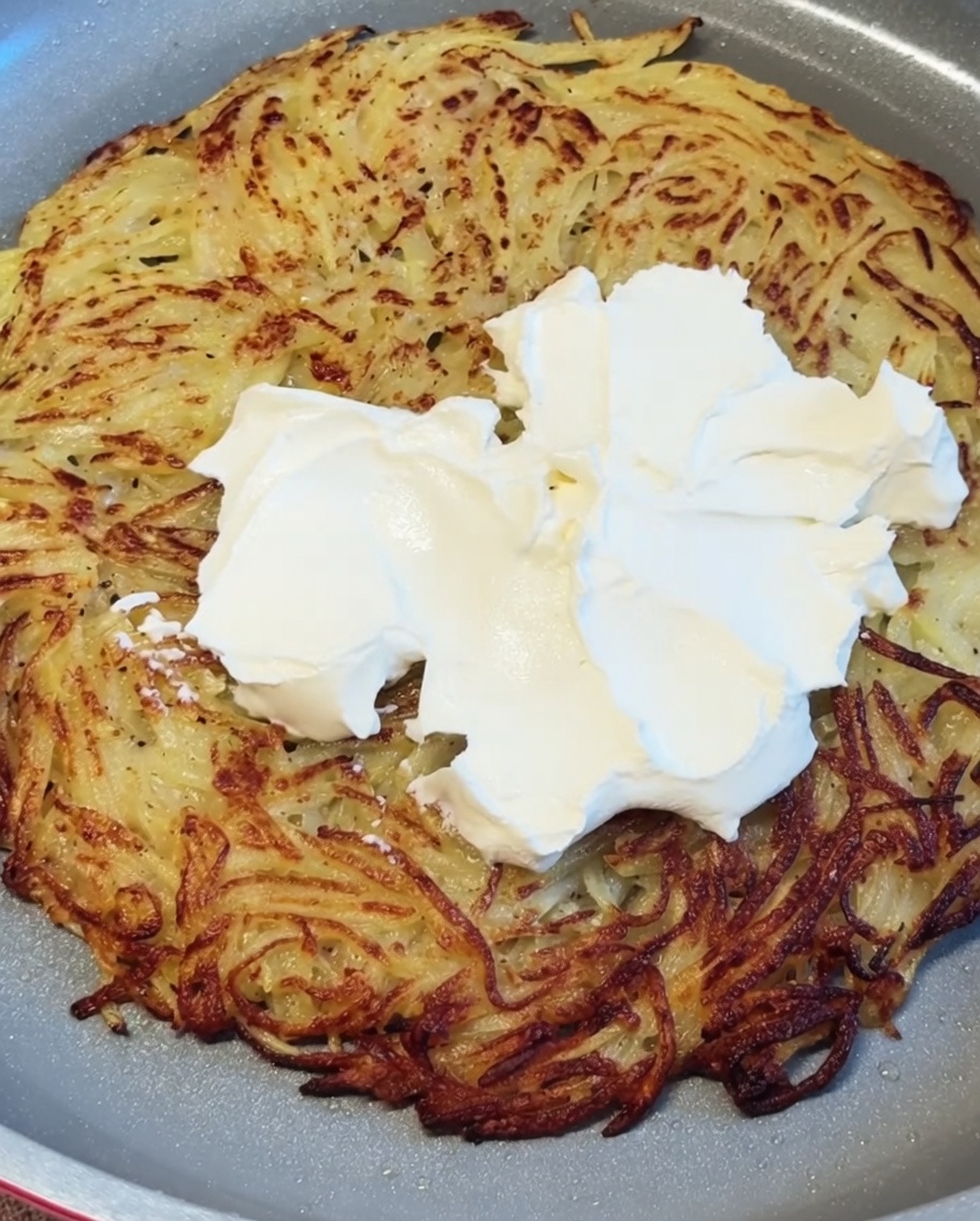 Du fromage à la crème blanc déposé en cuillerées et lissé sur la galette de pommes de terre chaude et croustillante.