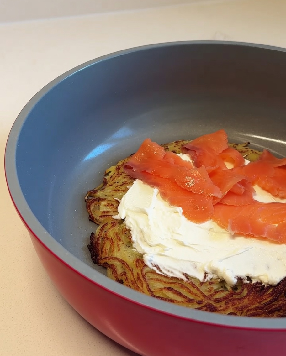 Des tranches de saumon fumé rose superposées sur la couche de fromage à la crème sur la base de la pizza aux pommes de terre.