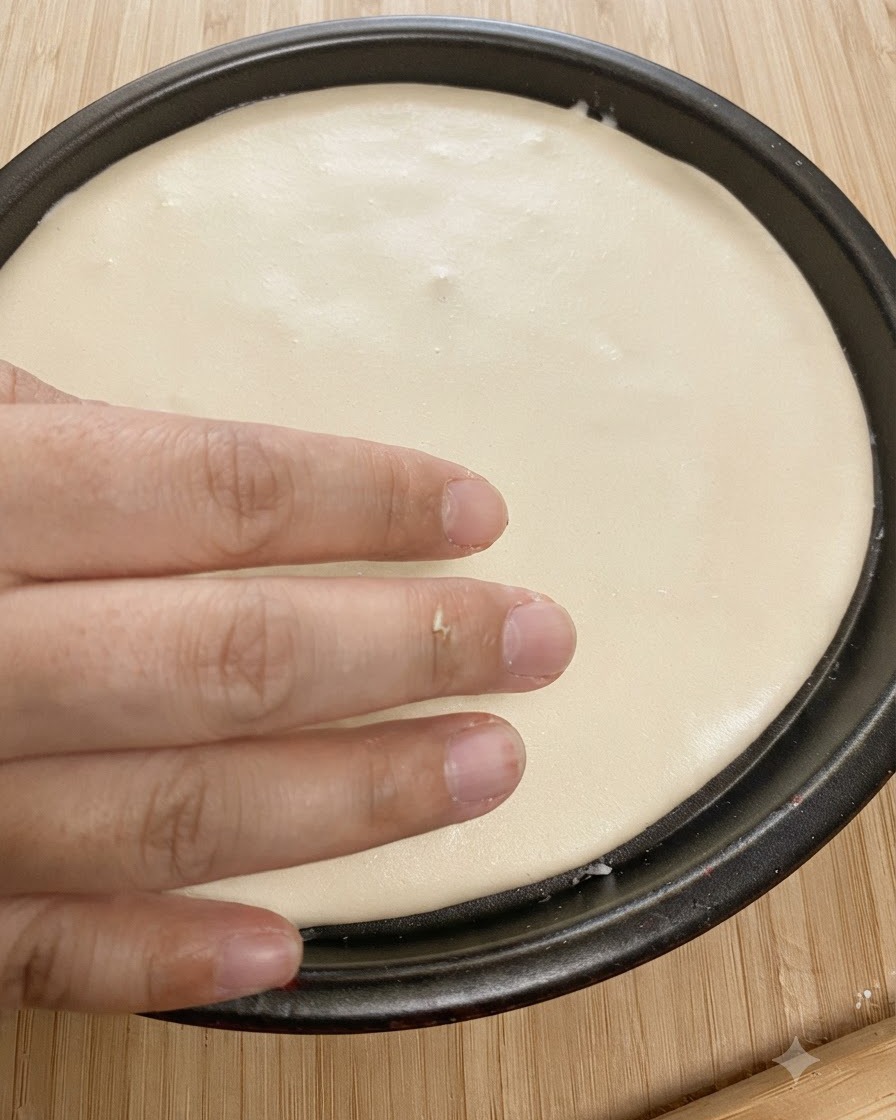 Pâte ronde aplatie ajustée dans un plat de cuisson noir avec une main appuyant sur les bords.