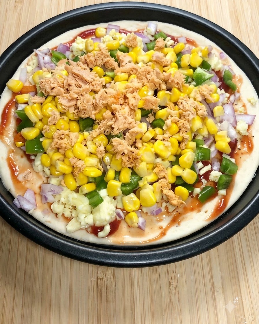 Une base de pizza ronde garnie de sauce tomate, de mozzarella, de poivrons verts, de maïs doux et de morceaux de saumon en conserve.