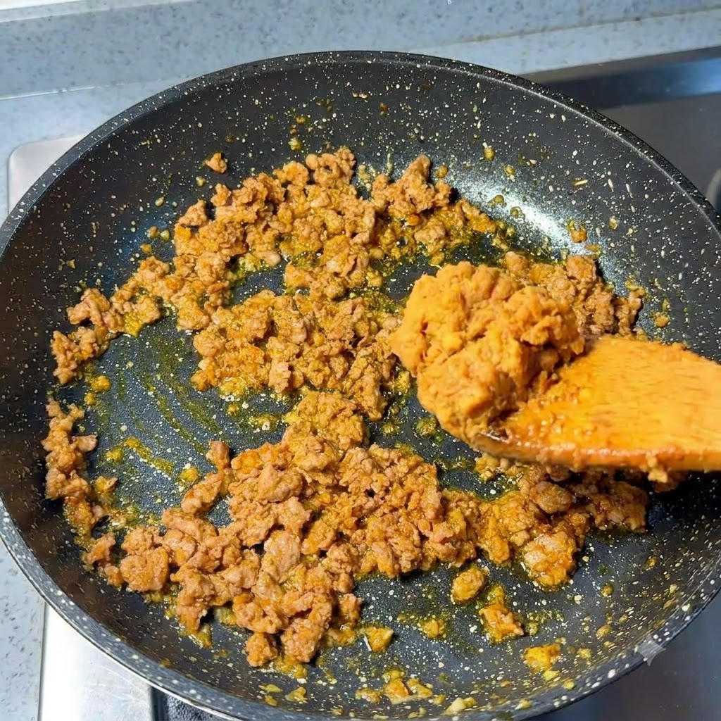 Une cuillerée de pâte miso ajoutée au porc haché sauté dans la poêle.