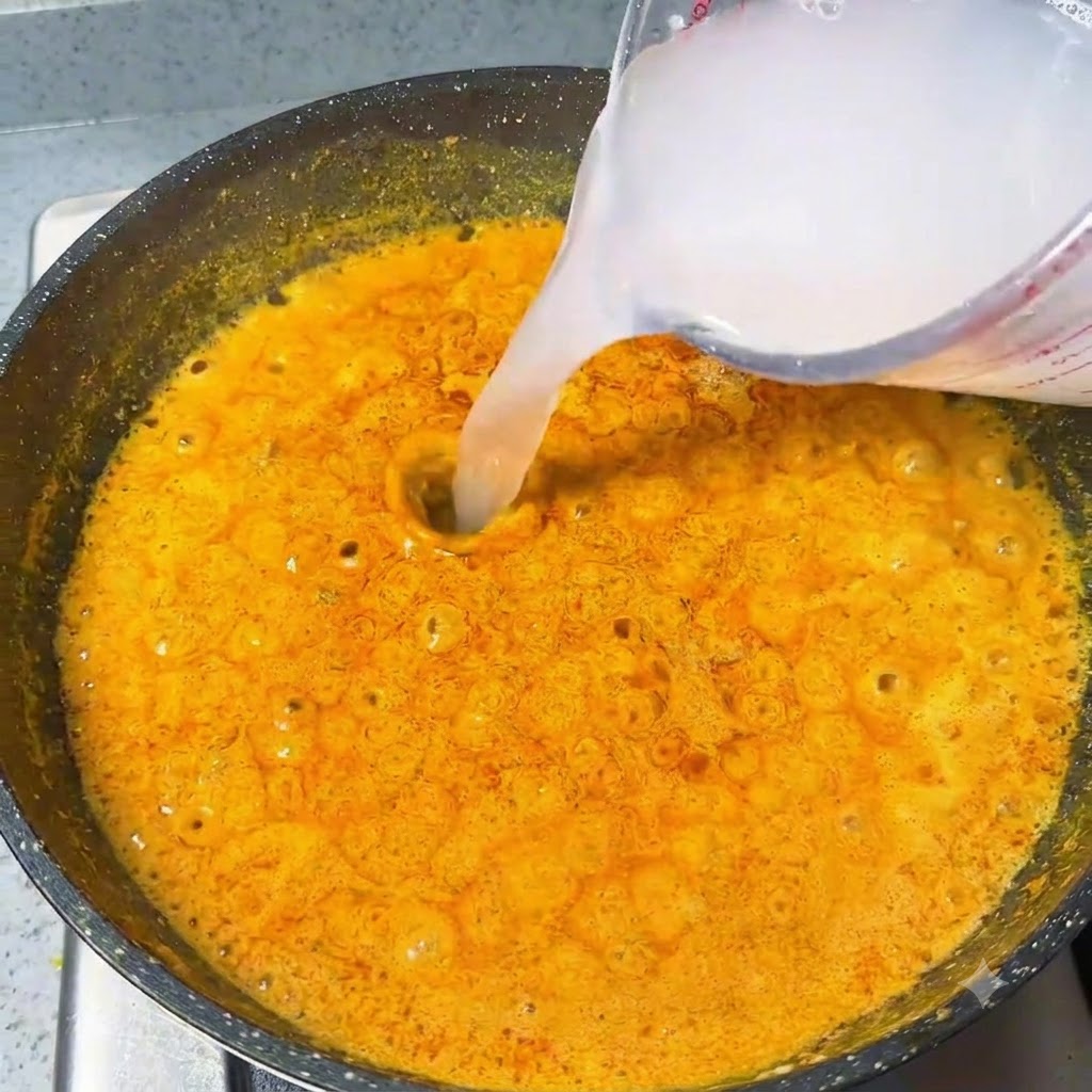De leau versée depuis un verre doseur dans une sauce au curry orange bouillonnante.