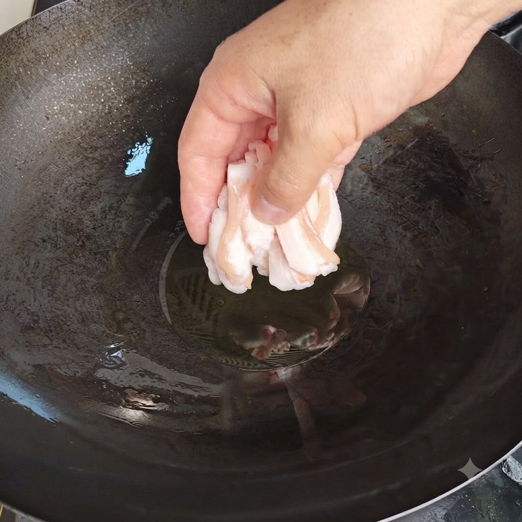 Une main déposant délicatement de fines tranches de graisse de porc crue dans un wok chaud avec de lhuile.