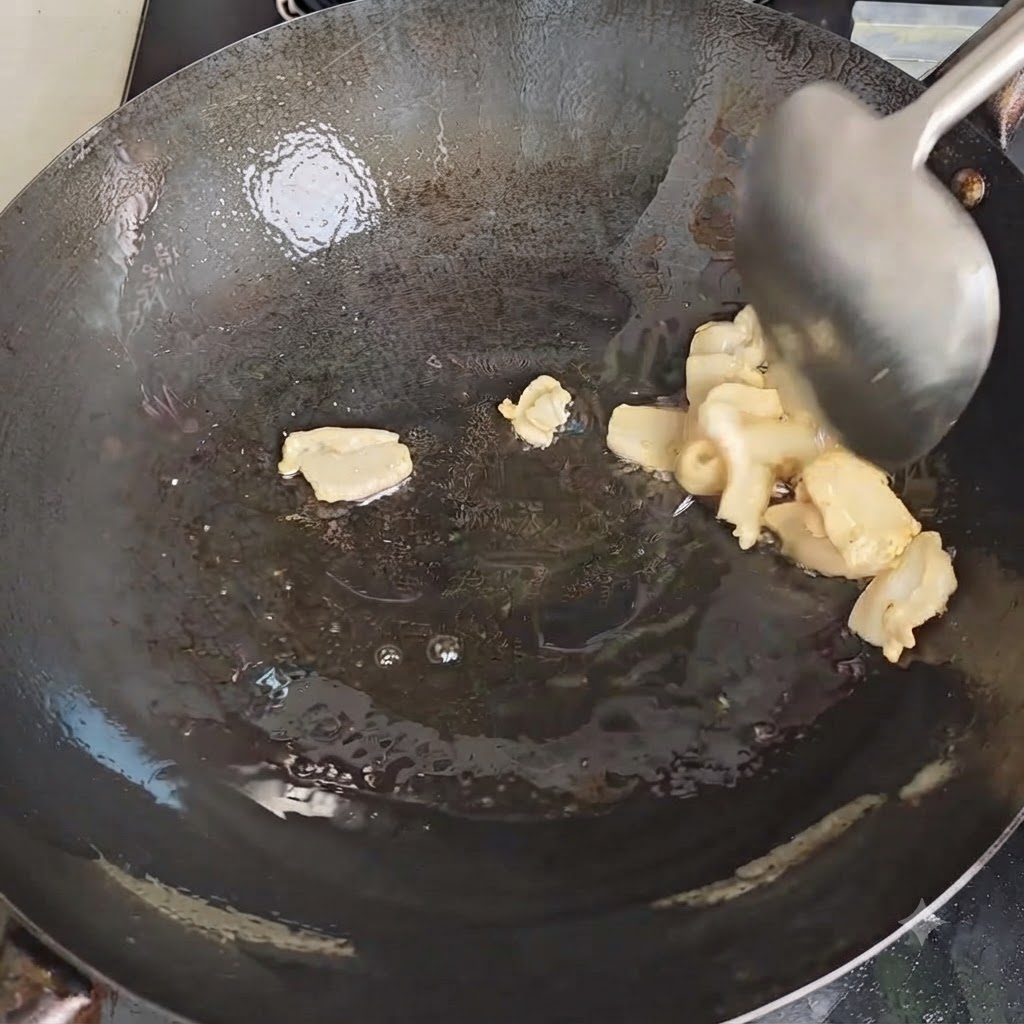 Une spatule en métal remuant des morceaux de graisse de porc pendant quils fondent dans un wok chaud.