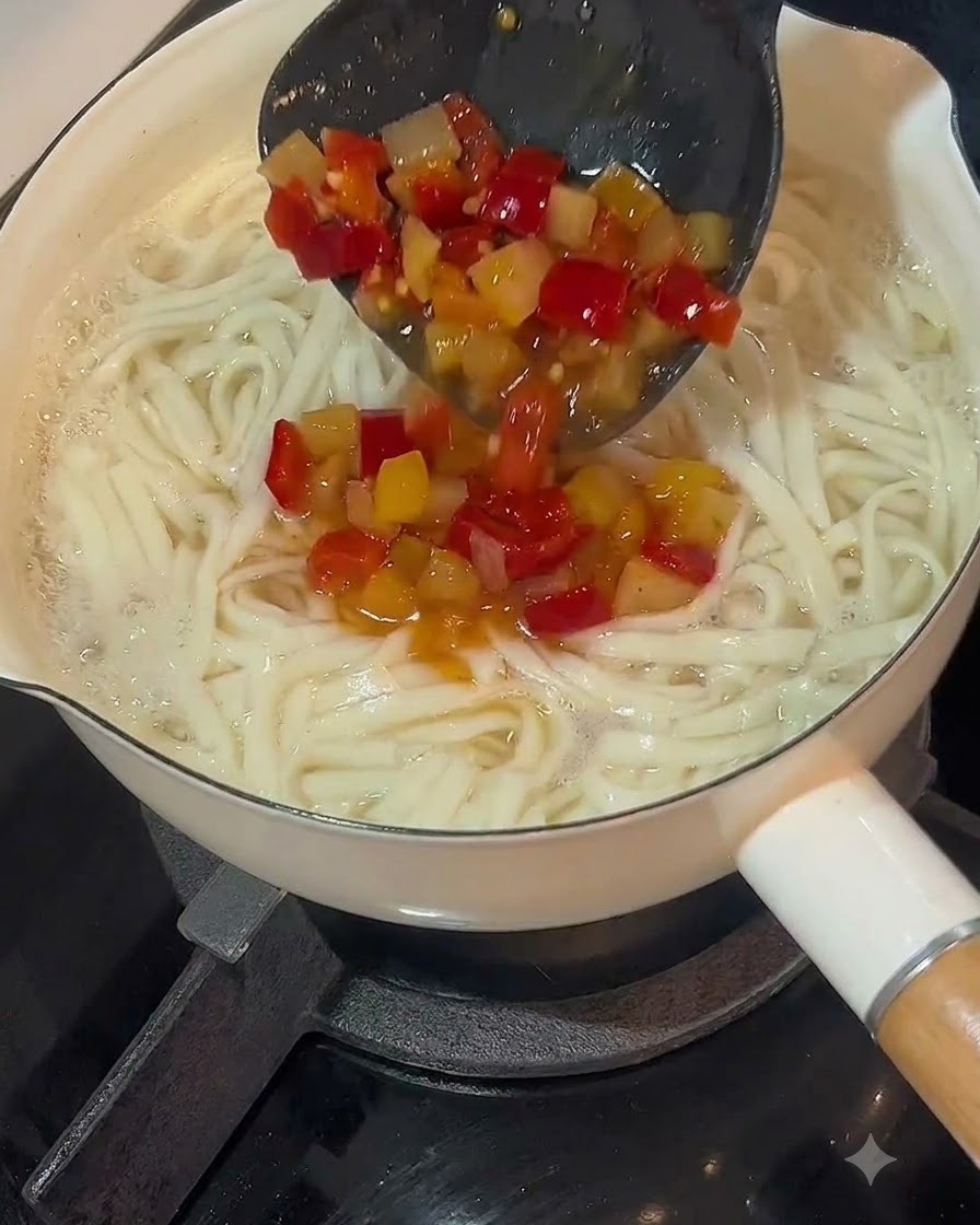 Une louche versant la base de soupe au piment pickelé sur une casserole de nouilles cuites.