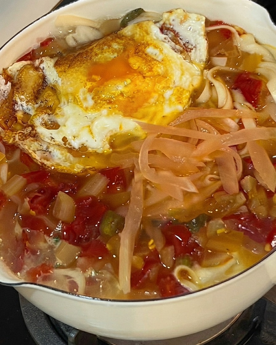 De la coriandre fraîche hachée saupoudrée sur le dessus dune casserole bouillonnante de nouilles, de chou pickelé et dun œuf frit.